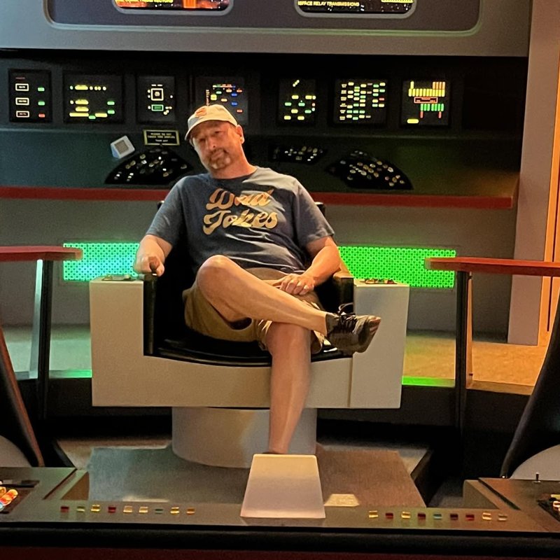 Jim Perri seated in a starship captain's chair, wearing a Dad Jokes t-shirt